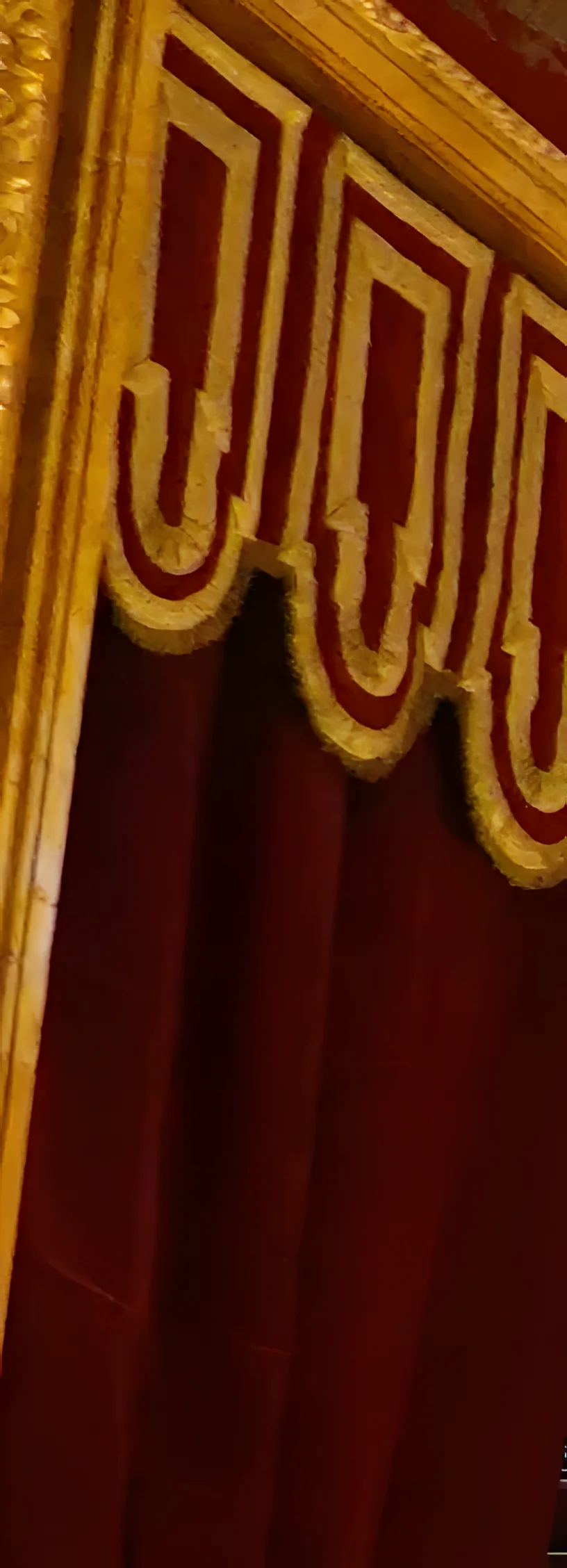 A portrait veiled in crimson velvet under a gold-fringed valance.